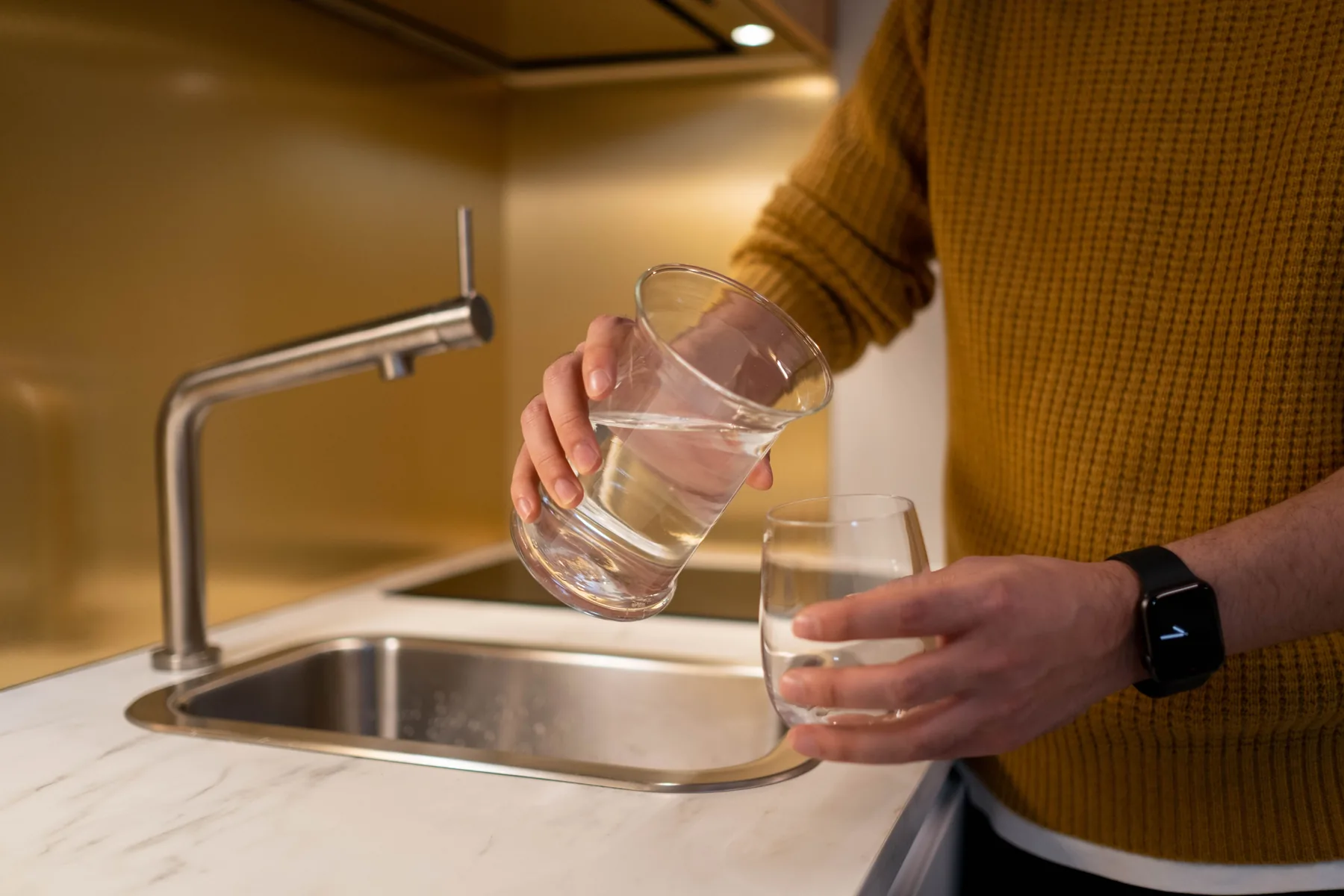 Person pouring clean water into a drinking glass in a kitchen